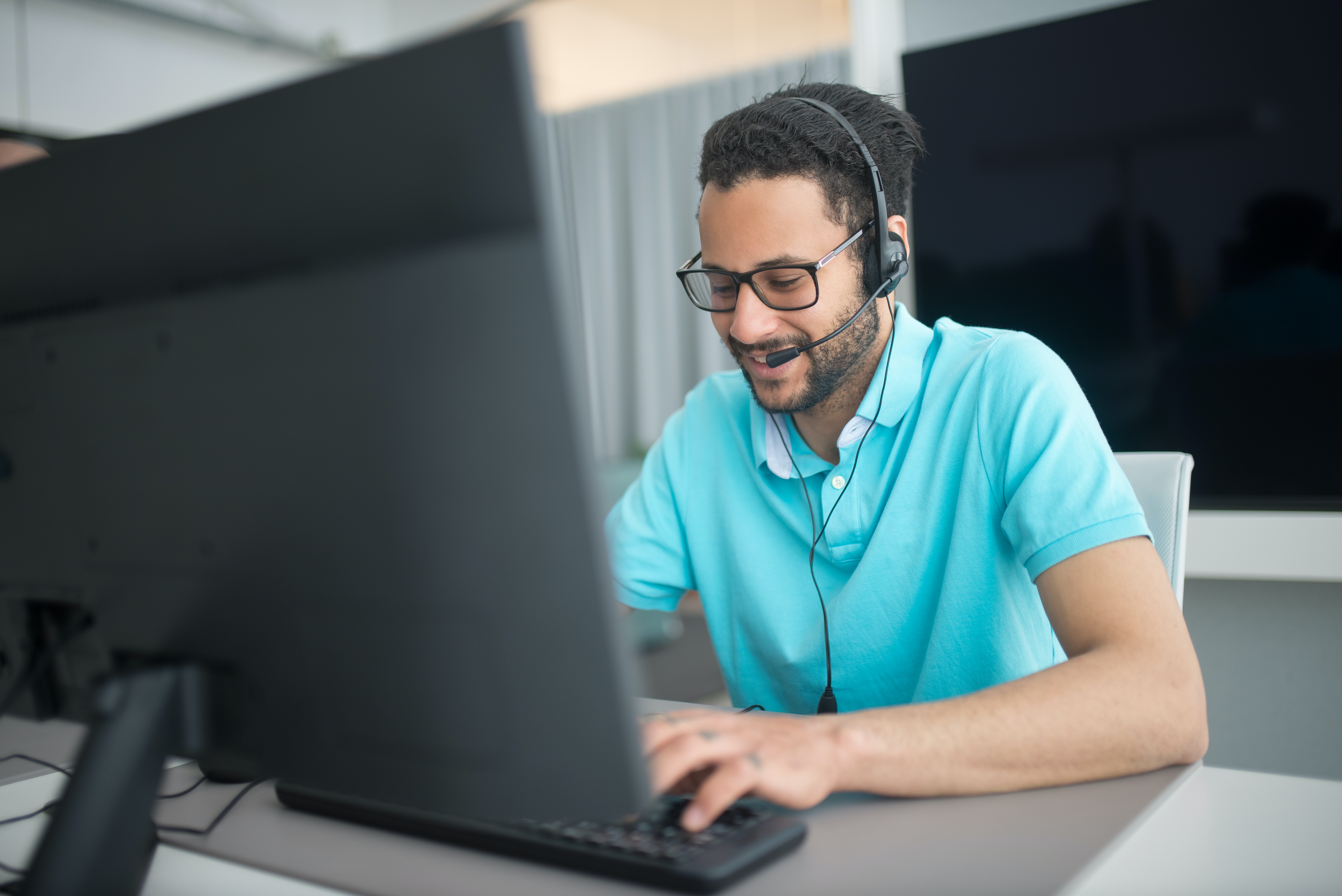 Man in Blue Polo Shirt with Headset Using Computer